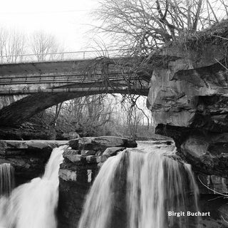 Black and white photograph of a bridge over a waterfall with rocky cliffs.
