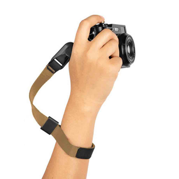 A hand holding a camera attached to a brown camera strap with black adjustment elements.