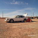 Car with open hood on a dirt road under a blue sky, with a colorful kite on the ground.