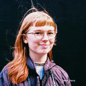 Person with red hair and glasses against a black background