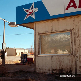 Abandoned gas station with a star logo on the roof, mountains in the background.
