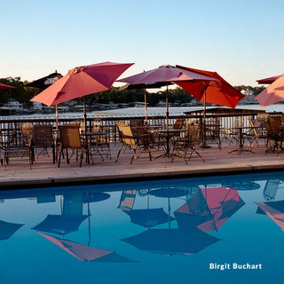 Outdoor dining area with red umbrellas and tables by a pool, featuring the photographer's name 'Birgit Buchart'.