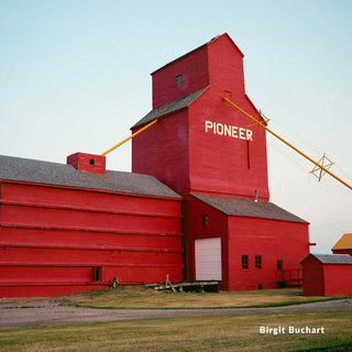 Red grain elevator with 'Pioneer' branding on a clear day, featuring the photographer's name.
