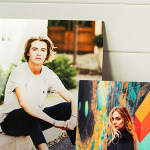 Two metal prints with one featuring a portrait of a man in a white shirt and the other an abstract colorful art piece.