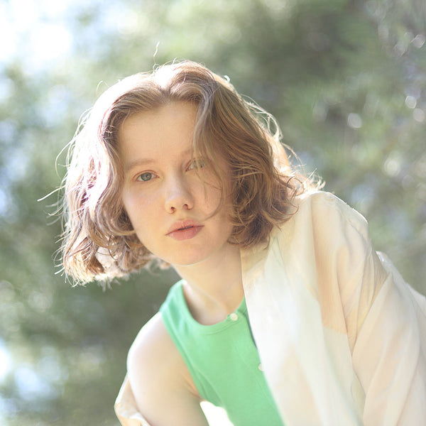 Person with shoulder-length hair wearing a green top and beige cardigan outdoors