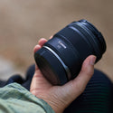 Hand holding a Canon camera lens with a blurred natural background