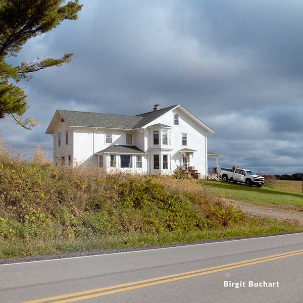 White house with a truck parked in front on a cloudy day, with 'Birgit Buchart' watermark.