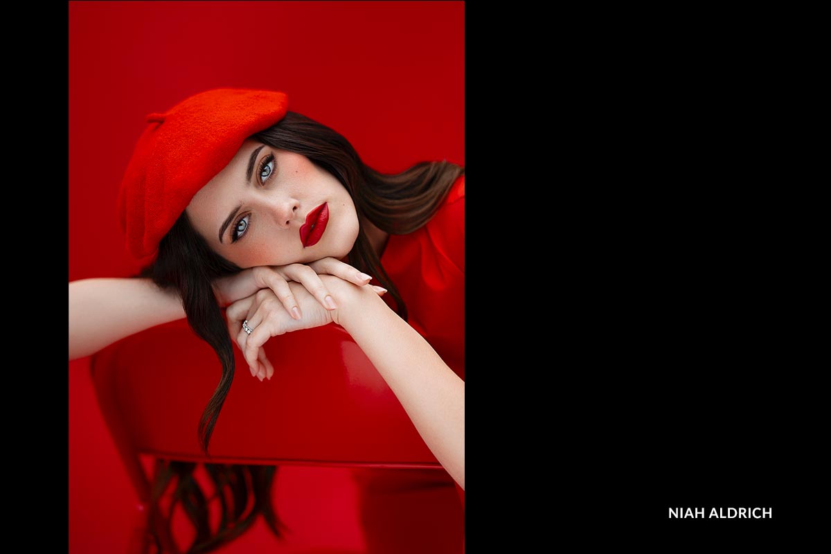 Woman wearing a red beret and lipstick against a red background, with 'Niah Aldrich' credited.