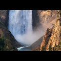 A dramatic landscape photograph of a large waterfall cascading down steep rocky cliffs into a river below, with mist rising and trees along the canyon edges.