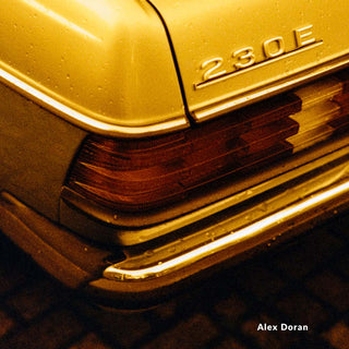 Close-up of a car's grille with '230E' badge, featuring a warm yellow tone.