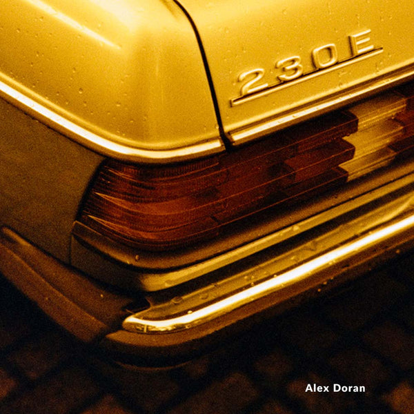 Close-up of a car's grille with '230E' badge, featuring a warm yellow tone.
