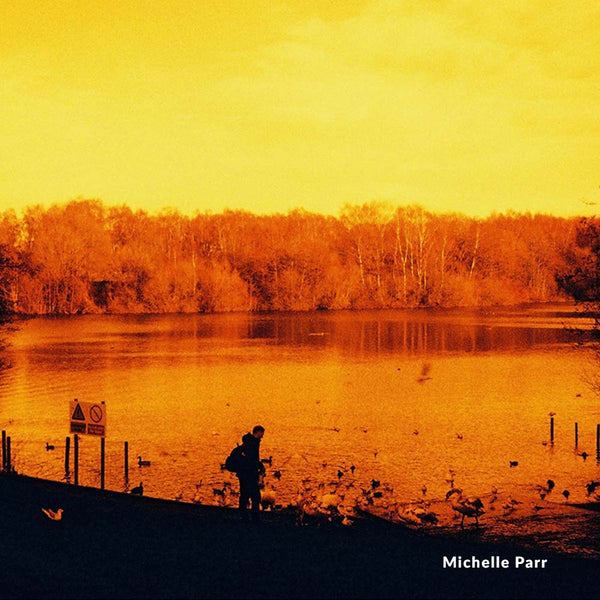 Two people standing by a lake at sunset with a warm orange color filter.