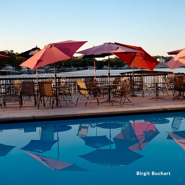 Outdoor dining area with red umbrellas and tables by a pool, featuring the photographer's name 'Birgit Buchart'.