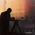 Silhouette of a person sitting at a table against a wooden wall with warm lighting.