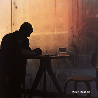 Silhouette of a person sitting at a table against a wooden wall with warm lighting.