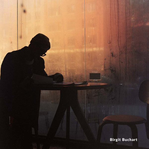Silhouette of a person sitting at a table against a wooden wall with warm lighting.