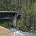Stone arch bridge over a river with dense forest on either side, featuring the photographer's name 'Birgit Buchart'.