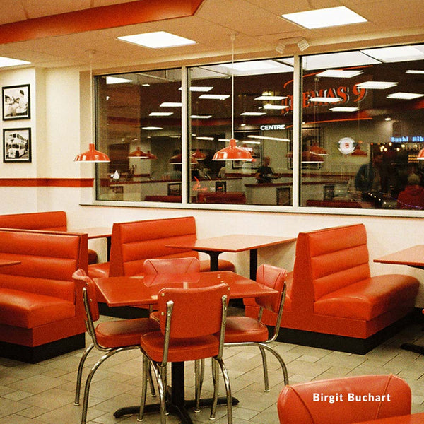 Diner interior with red booths and tables, featuring a large window.