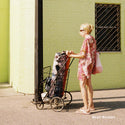 Woman in a pink dress pushing a vintage shopping cart against a green wall.